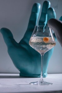 a glass of gin with an orange in it next to a blue hand