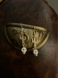 a pair of cactus skull earrings on a brass plate