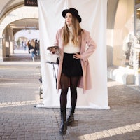 a woman in a pink coat and black tights posing in front of a building