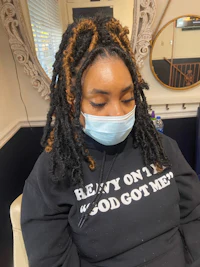 a woman with dreadlocks sitting in a chair wearing a face mask