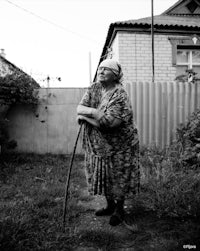 an old woman with a cane standing in a yard