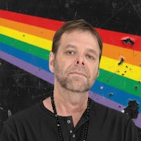 a man in a black shirt standing in front of a rainbow flag