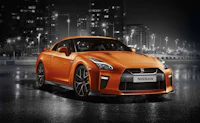 the orange nissan gt-r is parked in front of a city at night