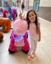 a little girl standing next to a pink stuffed animal