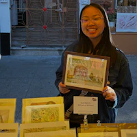 a woman holding a framed piece of art in front of a table