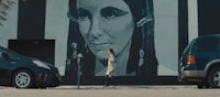 a woman walks past a mural of a woman on a wall