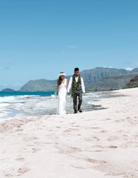 a bride and groom walking on the beach in hawaii