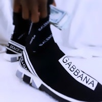 a person holding a pair of sneakers with the word gabbana on them