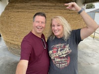 a man and woman pose for a selfie in front of a large hay bale