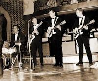a group of men in tuxedos playing guitars on stage