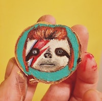 a person is holding a piece of wood with a painting of a sloth