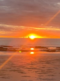 the sun is setting over a beach with a boat in the background