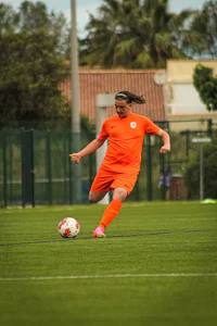 a woman in an orange uniform kicking a soccer ball