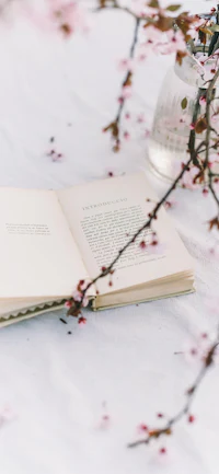 an open book on a table next to a branch of cherry blossoms