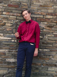 a man in a red shirt leaning against a stone wall