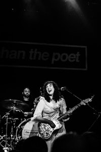 a woman on stage with a guitar in front of a black background