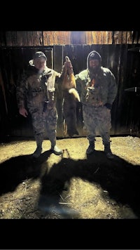 two men standing in front of a barn holding a deer