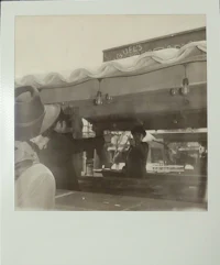 an old photograph of a man standing in front of a food stand