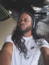 a man with long hair and headphones in front of a car