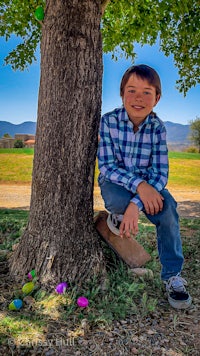 a boy leaning against a tree with easter eggs