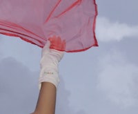 a person in white gloves is holding a red flag in the air