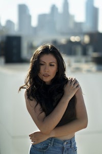 a woman posing on a rooftop with a city skyline in the background