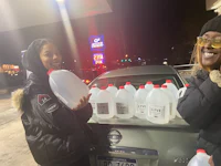 two women standing in front of a car with jugs of water