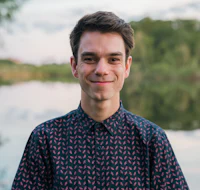 a young man smiling in front of a body of water