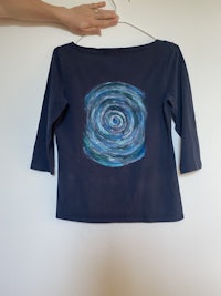 a hand is holding a blue shirt with a spiral on it
