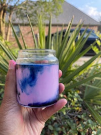 a hand holding a blue and purple scented candle