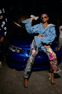 a woman is posing next to a blue car