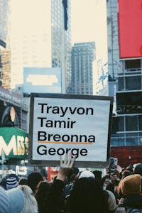 a group of people holding up a sign that says trayvon tamir brona george