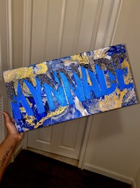 a person holding up a blue and gold painted name sign
