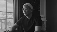 a black and white photo of a man sitting in front of a window