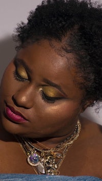 a black woman with gold eyeshadow and a necklace