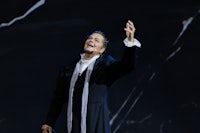 a man in a black coat is singing on stage