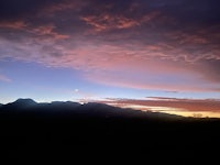 a sunset over a mountain range with mountains in the background
