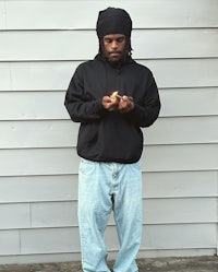 a man in a black hoodie and jeans standing next to a wall