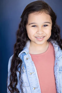 a young girl in a denim jacket smiling for the camera