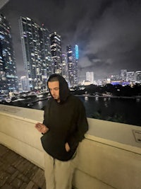 a man in a hoodie leaning against a wall at night