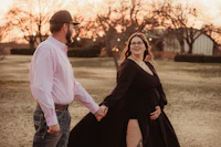 a pregnant couple holding hands in a field at sunset