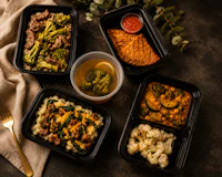four black plastic containers with food and utensils on a table