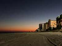 a beach at dusk with buildings in the background