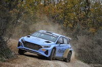 a blue rally car driving down a dirt road