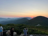 people standing on top of a mountain watching the sun set