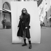 a woman in a black coat standing in front of a wall