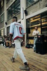 a man wearing a baseball jersey walks on a wooden floor