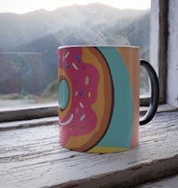 a coffee mug with a donut on it sits on a window sill