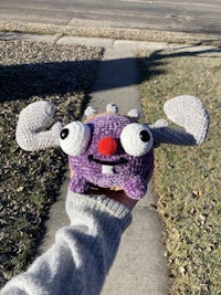 a person holding a crocheted purple monster doll