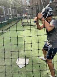 a young boy swinging a bat in a baseball batting cage